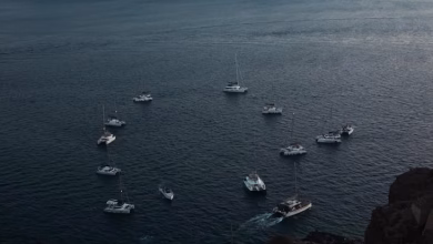 غروب الشمس فوق منازل أويا البيضاء ذات القباب الزرقاء في سانتوريني مع إطلالة على بحر إيجه والعمارة اليونانية الساحلية الرومانس