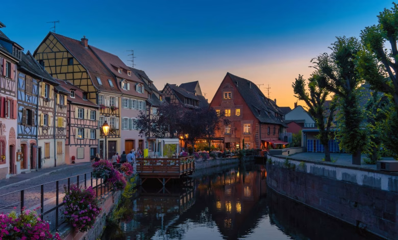 A charming European old town with colorful historic buildings, cobblestone streets, a riverside promenade, and a scenic castl