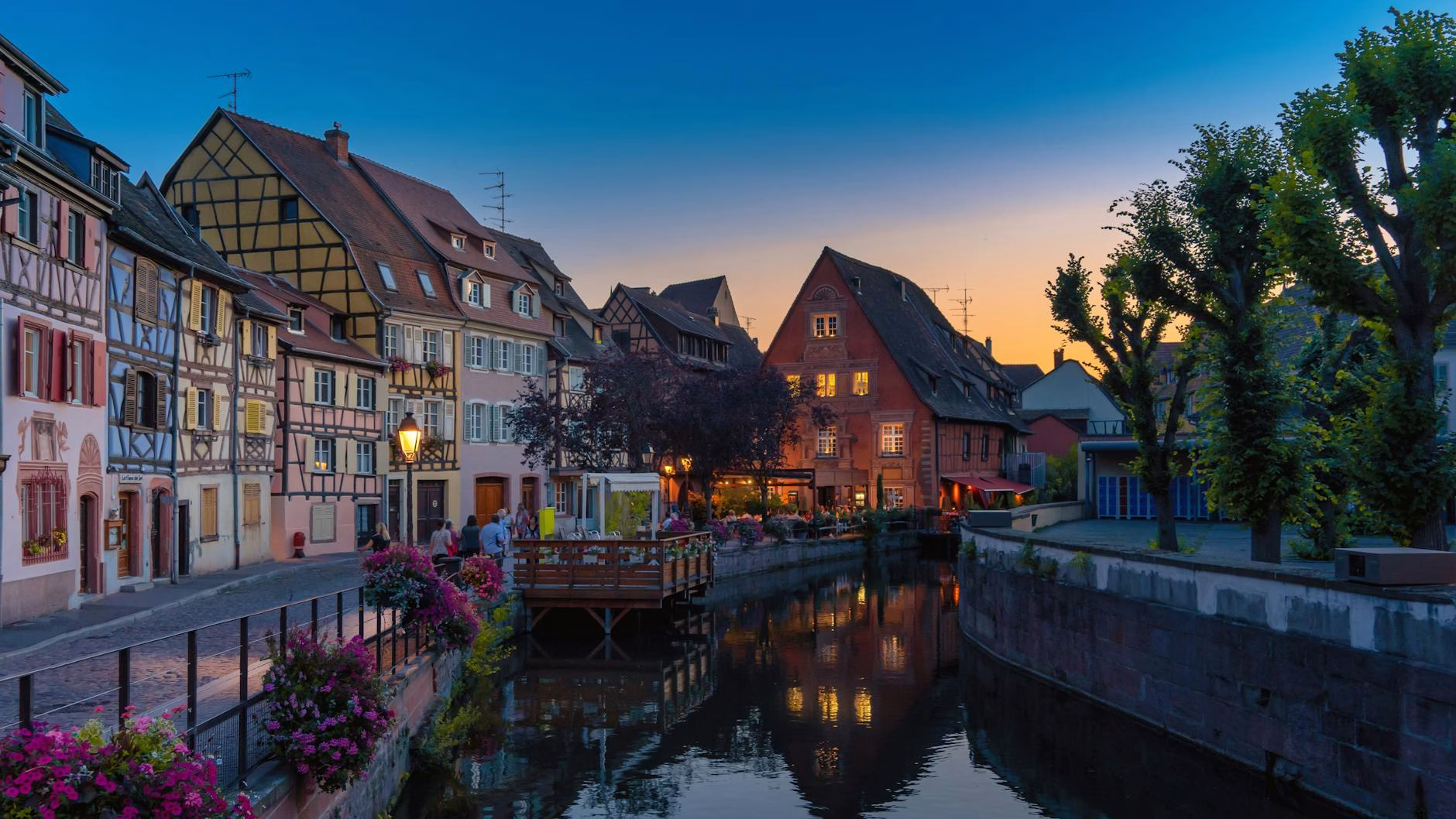 A charming European old town with colorful historic buildings, cobblestone streets, a riverside promenade, and a scenic castl